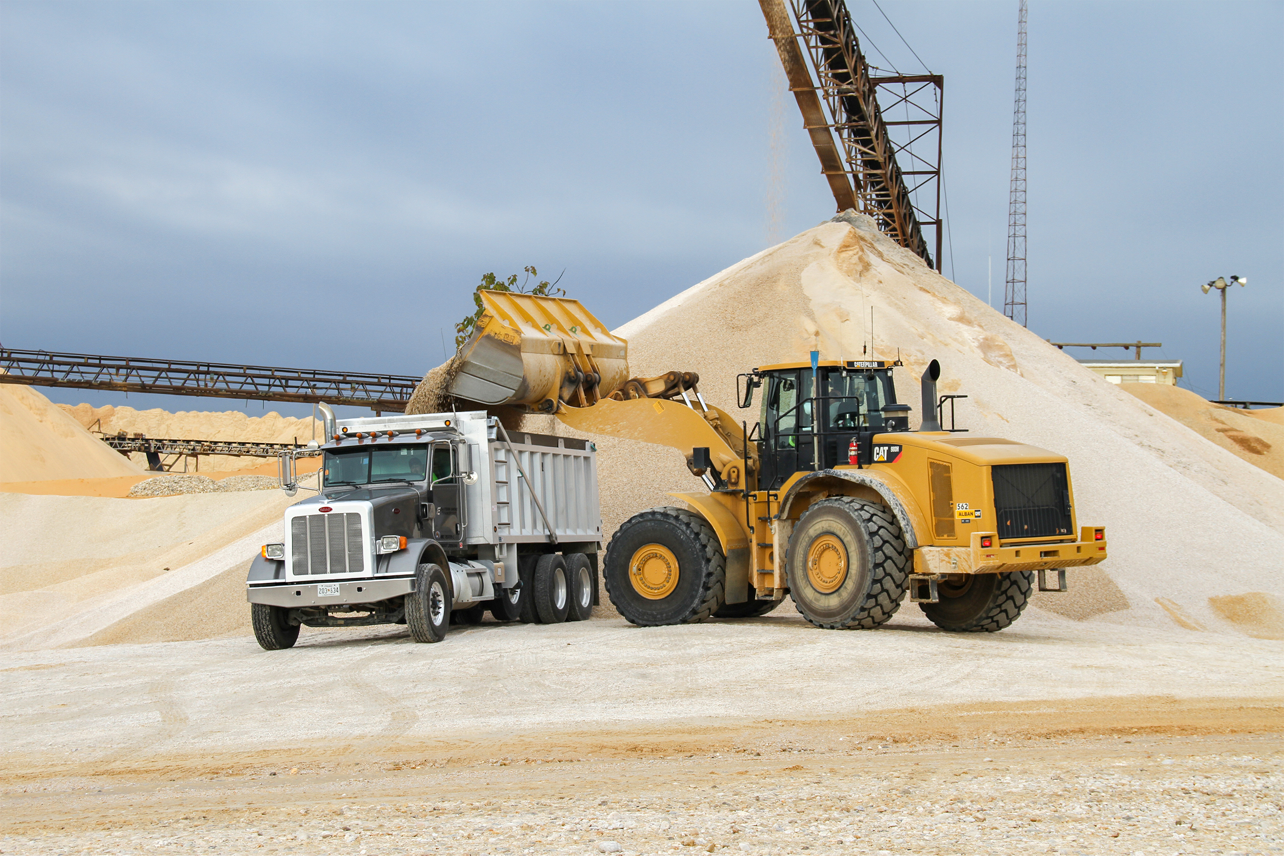 Yellow CAT Loader machine filling a gray dump truck with sand at an aggregate construction site