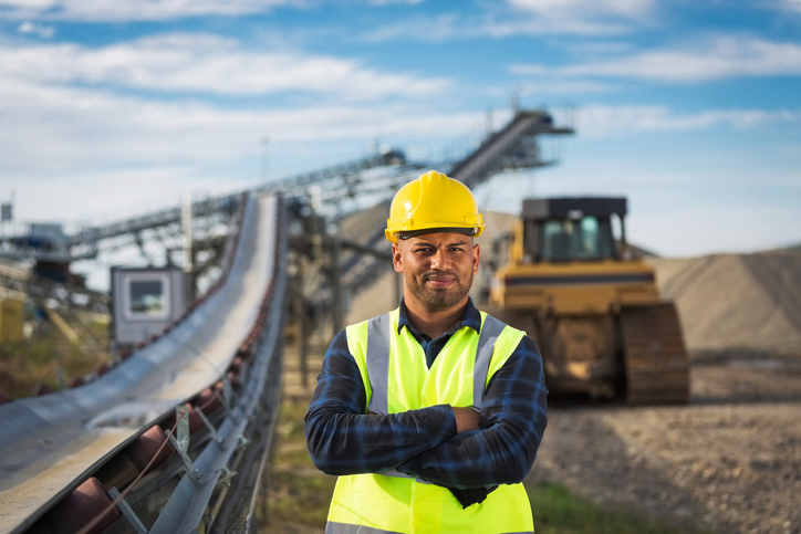 Construction worker in safety vest and helmetstanding confidently with arms crossed at a construction site