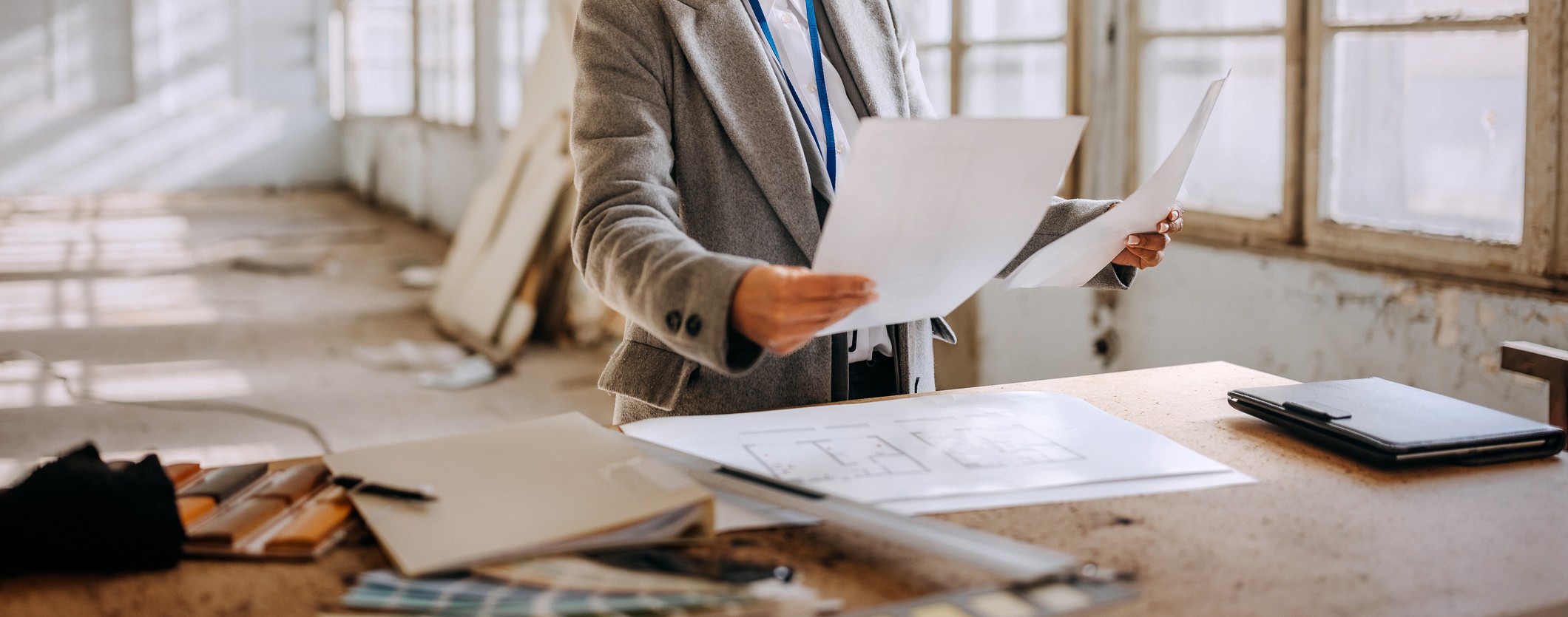 Person in suit reviewing architectural blueprints and papers for construction planning in a building under construction.