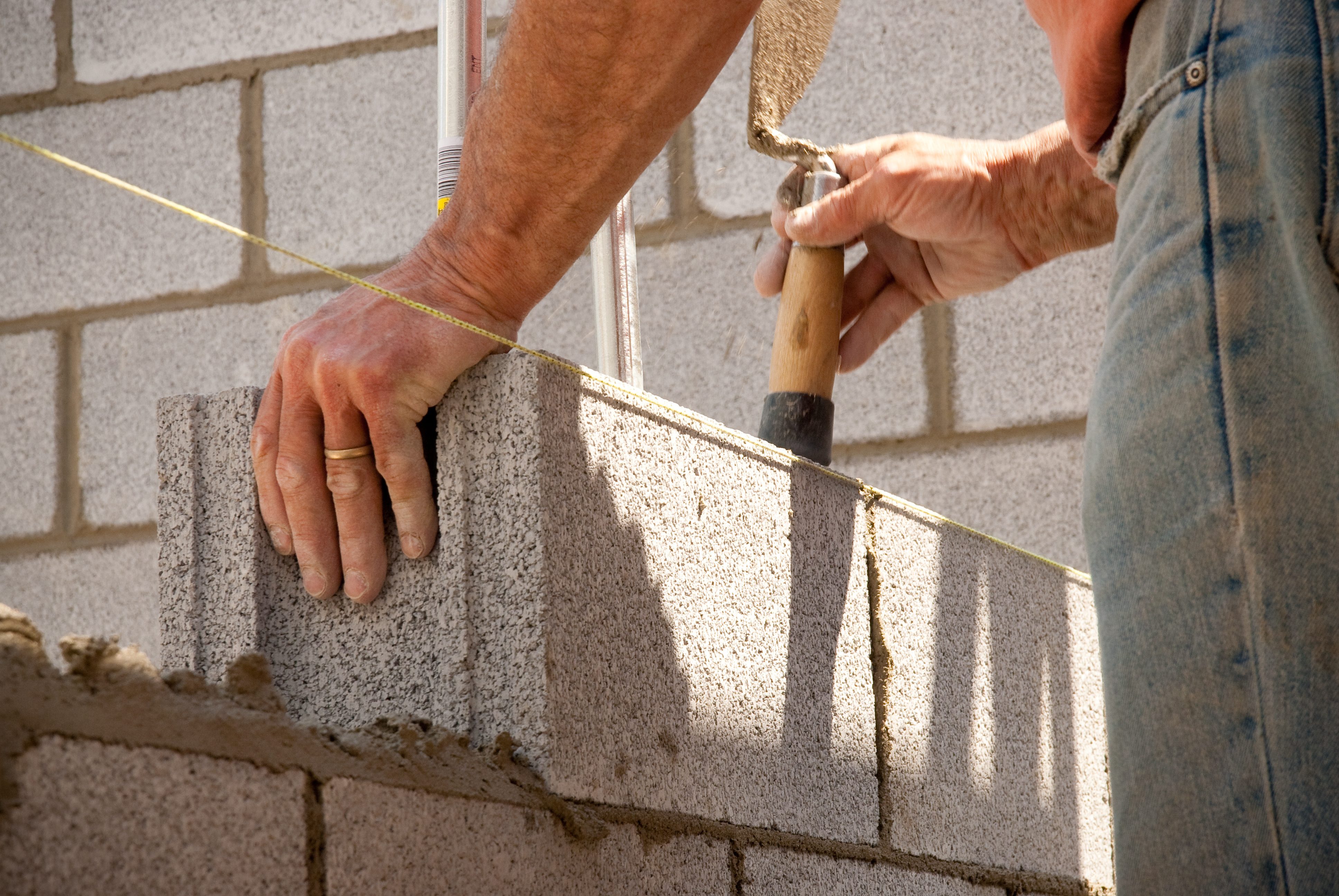 Construction worker in blue jeans applying mortar to fill gaps between bricks